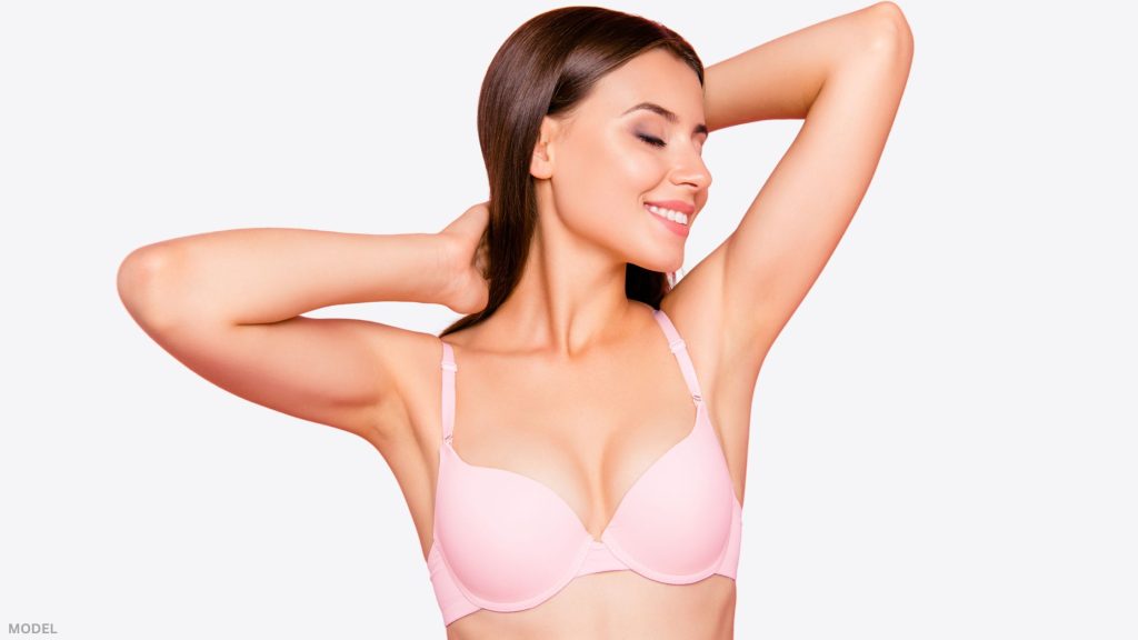 Woman in bra reaching up with hands behind head and eyes closed (model)